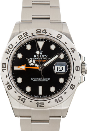 A Rolex Explorer 2 watch with a stainless steel bracelet, black dial, black bezel with white indices, and an orange GMT hand.